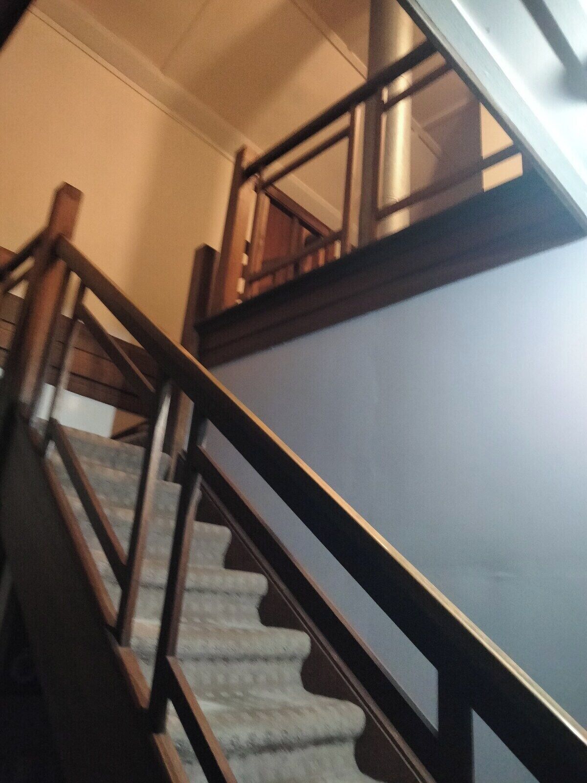 Un escalier avec des rampes et une main courante en bois, menant à l’étage supérieur.