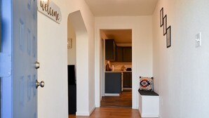 A hallway with a blue door, a welcome sign, a bench with a patterned cushion, and a kitchen area in the background. - Relax & Feel At Home During Your Pittsburgh Stay (Pittsburgh)