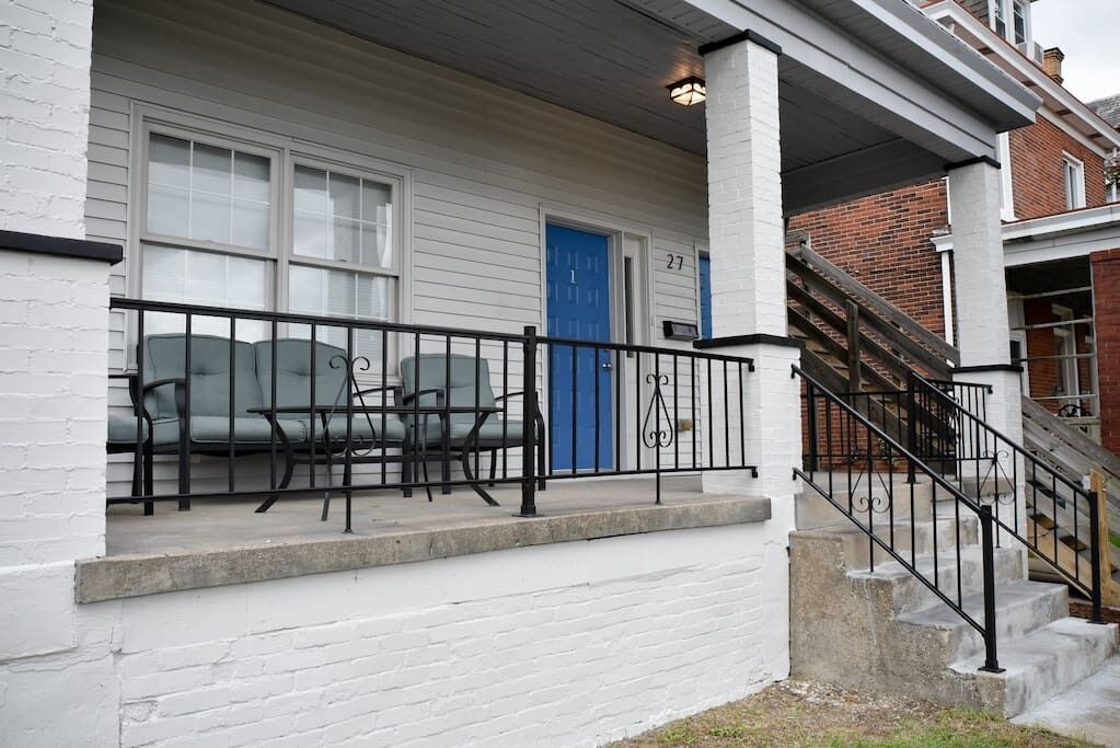 A white building with a blue door, numbered 27, and a staircase with a black railing.