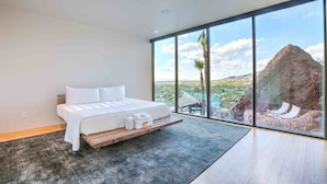 Une chambre moderne avec un grand lit, une plateforme en bois et une vue sur un paysage montagneux grâce à de grandes fenêtres du sol au plafond.