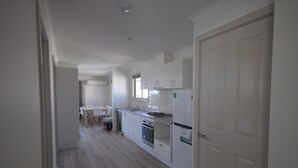 A modern kitchen with white cabinetry, a dining area with a table and chairs, and a door leading to another room. - Dylene Caravan Park - 2 Br Family Cabin With Air (Portarlington)