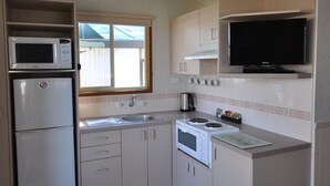 A compact kitchen with a microwave, stove, sink, and a television mounted above the counter. - Dylene Caravan Park - 2 Br Family Cabin With Air (Portarlington)