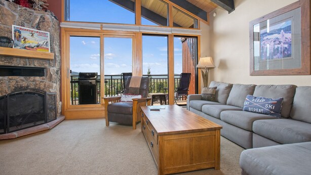 A cozy living room with a fireplace, large windows, a wooden coffee table, and a gray sofa. - Walk to Gondolas! Heated Pool & Hot Tubs - Perfect for 2 couples & 2-4 singles or kids (Steamboat Springs)