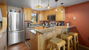 A modern kitchen with wooden cabinets, stainless steel appliances, granite countertops, and bar stools. - Walk to Gondolas! Heated Pool & Hot Tubs - Perfect for 2 couples & 2-4 singles or kids (Steamboat Springs)