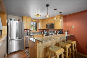 A modern kitchen with wooden cabinets, stainless steel appliances, granite countertops, and bar stools.