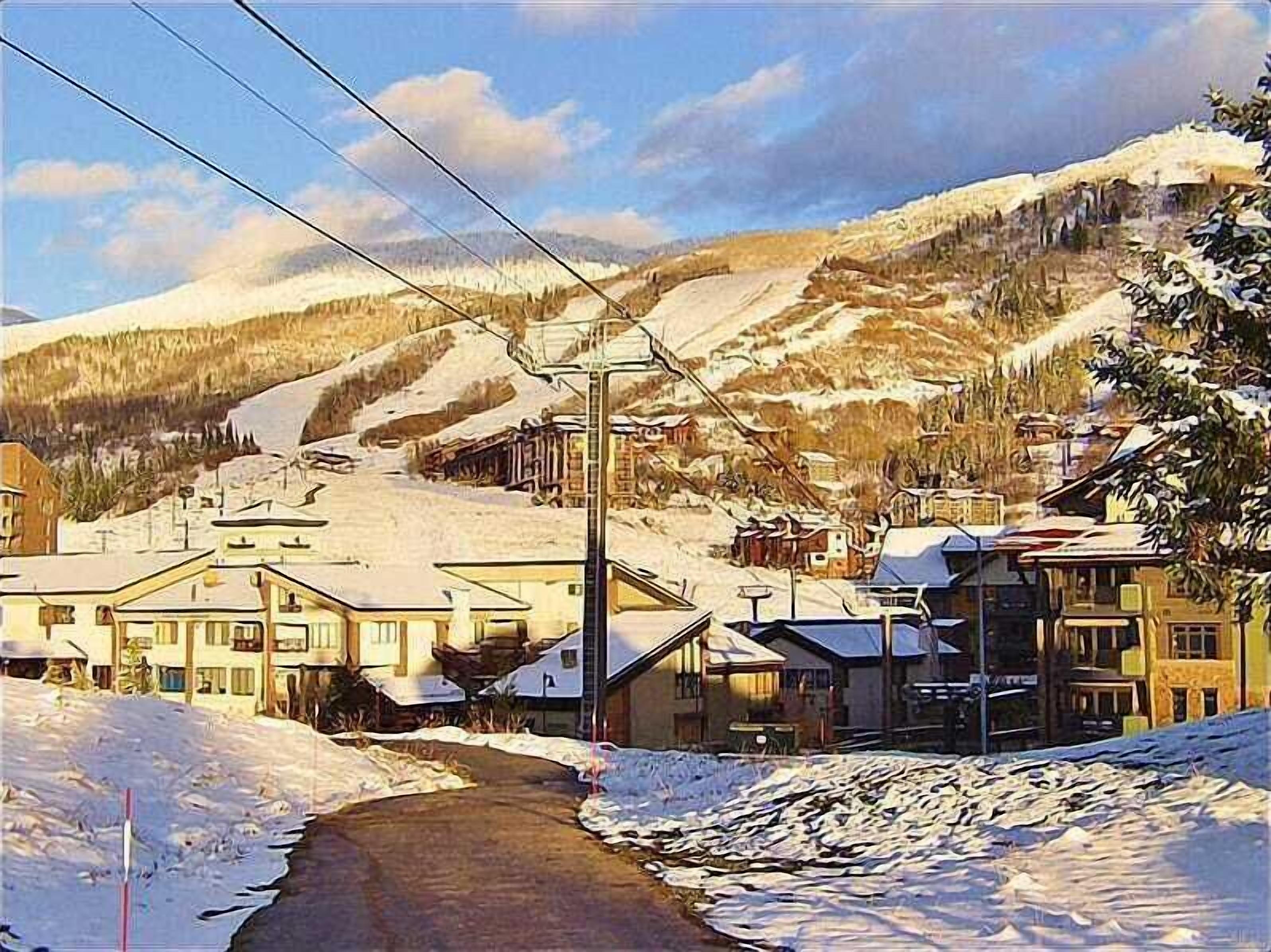 Une ville de montagne enneigée, avec des bâtiments, une piste de ski et une route.