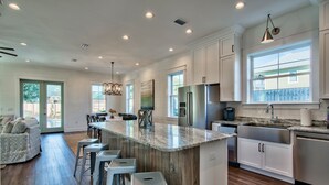 A modern kitchen with a large island, bar stools, stainless steel appliances, and a view of the backyard. - Beachin' *HeatedPool&Spa*Golf Cart*Bikes*BeachSvc* (Destin)
