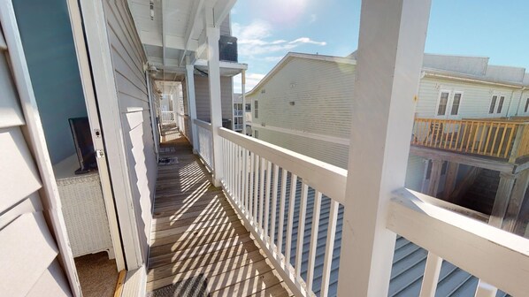 A covered outdoor balcony with a wooden floor and white railings, overlooking neighboring houses.