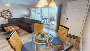 A living room with a dark brown sofa, a glass coffee table, wicker chairs, and a ship's wheel decoration. - Ocean View Condo w/ Private Balcony, Easy Beach Access (Tybee Island)