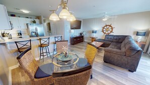 A modern living room with a dining area, a sofa, and a kitchen in the background. - Ocean View Condo w/ Private Balcony, Easy Beach Access (Tybee Island)