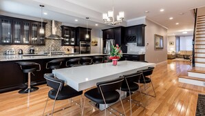 A modern kitchen with dark cabinets, a large island, and a chandelier. - UltraLuxe Apt in Boston Brownstone in Prime Area (Brookline)