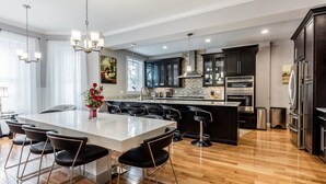 A modern kitchen with a large island, dark cabinetry, stainless steel appliances, and a wooden floor. - UltraLuxe Apt in Boston Brownstone in Prime Area (Brookline)