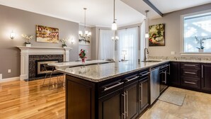 A modern kitchen with a large island, dark cabinetry, and a fireplace. - UltraLuxe Apt in Boston Brownstone in Prime Area (Brookline)