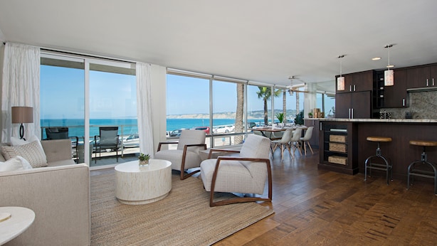 Amplia sala de estar con un ventanal grande con vistas al océano, una cocina con muebles oscuros de madera y una zona de bar con taburetes.