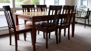 Een eettafel met zes stoelen, een kroonluchter en uitzicht op bomen door het raam.