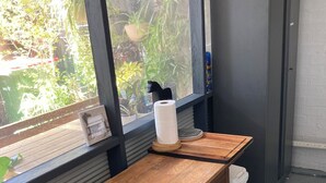 Una mesa de madera con un cubo de basura blanco y un marco de fotos en una habitación con ventana que da a follaje.