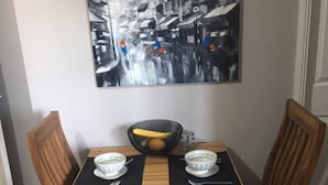 Una mesa de comedor con dos sillas, un cuenco de fruta y dos cuencos sobre individuales negros.