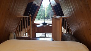 Un dormitorio acogedor en el ático con cama, ventilador de techo y vistas al exterior.