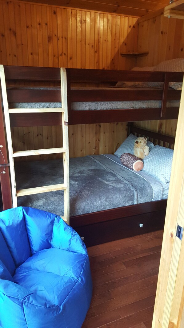 Un lit superposé avec une échelle, un fauteuil en forme de poire bleu et un ours en peluche sur le lit.