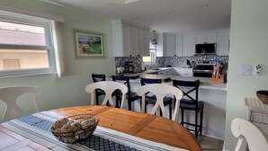A modern kitchen with white cabinets, a dining area with a wooden table and chairs, and a view through a window. - Treasure Island Escape is Calling... Many Family Friendly amenities for Fun! (Treasure Island)