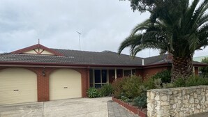 A two-story house with a garage, a stone wall, and a palm tree. - Torquay Shores - Family, Friends, Pets Welcome! (Torquay Surfcoast)