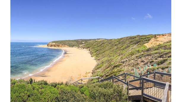 A coastal landscape with a sandy beach, a wooden staircase leading down to the beach, and a clear blue sky. - Torquay Shores - Family, Friends, Pets Welcome! (Torquay Surfcoast)