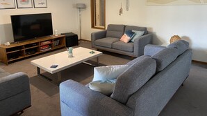 A living room with a flat-screen TV, grey sofas, a coffee table, and wall art including a beach scene. - Torquay Shores - Family, Friends, Pets Welcome! (Torquay Surfcoast)