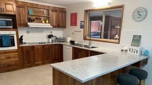 A kitchen with wooden cabinets, a granite countertop, a built-in oven, a microwave, a toaster, and a window overlooking a street. - Torquay Shores - Family, Friends, Pets Welcome! (Torquay Surfcoast)