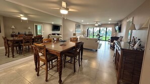 A spacious living area with a dining table, chairs, a sofa, and a TV mounted on the wall. - New Listing! Ground floor, easy access to the pool and beach! Siesta Dunes 2-104 (Siesta Key)