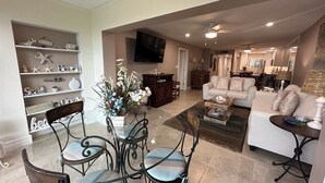 A spacious living room with a white sofa, a dining table with chairs, and a decorative wall with shelves. - New Listing! Ground floor, easy access to the pool and beach! Siesta Dunes 2-104 (Siesta Key)