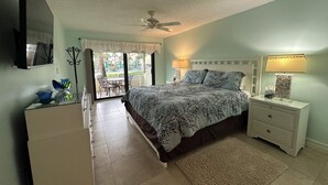A bedroom with a bed, bedside tables, a ceiling fan, and a view of an outdoor area with a table and chairs. - New Listing! Ground floor, easy access to the pool and beach! Siesta Dunes 2-104 (Siesta Key)