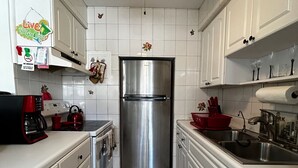 Eine Küche mit weißen Schränken, einem Edelstahlkühlschrank, einem Deckenventilator und einem gefliesten Boden.