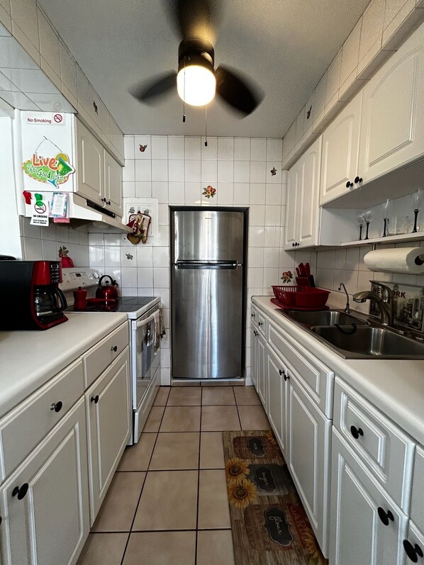 A kitchen with white cabinets, a stainless steel refrigerator, a ceiling fan, and a tiled floor.