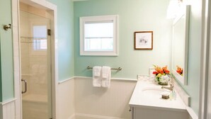 A bathroom with a glass shower door, a white sink, a mirror, and a small window. - Spacious and Updated 2 Bedroom Condo in the Heart of Newport (Newport)