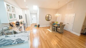 A spacious kitchen with a marble countertop, wooden flooring, and a dining area with wicker chairs and a chandelier. - Spacious and Updated 2 Bedroom Condo in the Heart of Newport (Newport)
