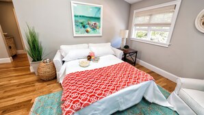 A bedroom with a bed, a window with blinds, a painting on the wall, and a plant. - Spacious and Updated 2 Bedroom Condo in the Heart of Newport (Newport)