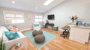 A spacious living room with a sofa, ottomans, and a coffee table. There is a kitchen area with a sink and a dining table. - Spacious and Updated 2 Bedroom Condo in the Heart of Newport (Newport)