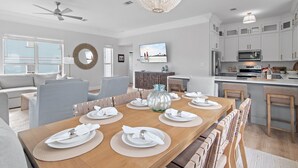 Une cuisine moderne avec des meubles blancs, un four à micro-ondes et un coin repas agrémenté d’assiettes et de serviettes blanches.