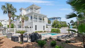 Une maison à deux étages avec une piscine, un espace salon extérieur et des palmiers.