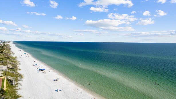 Une plage avec une eau d’un bleu limpide, du sable blanc et quelques parasols.