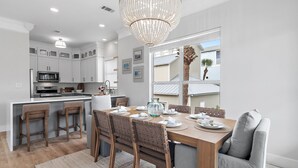 Une cuisine moderne avec des meubles blancs, un îlot central et un coin repas comprenant une table et des chaises en bois.
