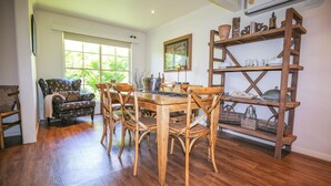 A dining area with a wooden table and chairs, a rustic wooden shelf with kitchenware, and a window with a view of greenery. - ABBEVILLE IN BRIGHT: Bright (Bright)