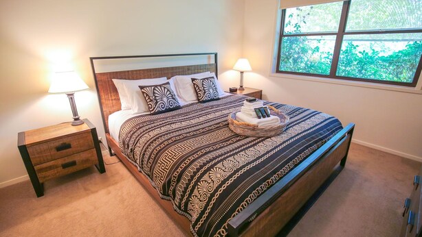A neatly made bed with patterned bedding, two bedside tables with lamps, and a window with a view of greenery. - ABBEVILLE IN BRIGHT: Bright (Bright)