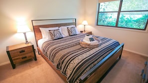 A neatly made bed with patterned bedding, two bedside tables with lamps, and a window with a view of greenery.