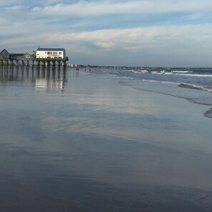 A beach with a pier extending into the water, a building labeled "restaurant" on the pier, and a distant shoreline with buildings.