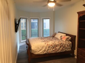 Quarto com cama, ventilador de teto e vista para uma varanda.