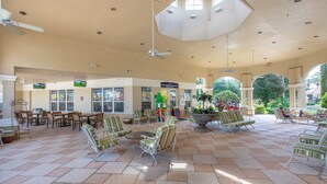 A spacious indoor area with tiled flooring, multiple seating arrangements, ceiling fans, and a variety of shops in the background. - Luxury 5 Star Vacation Villa- Free WiFi & Long Distance (Kissimmee)