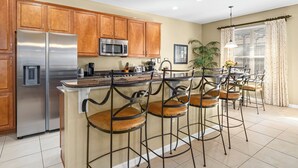 A kitchen with wooden cabinets, stainless steel appliances, and a bar area with metal stools. - Luxury 5 Star Vacation Villa- Free WiFi & Long Distance (Kissimmee)
