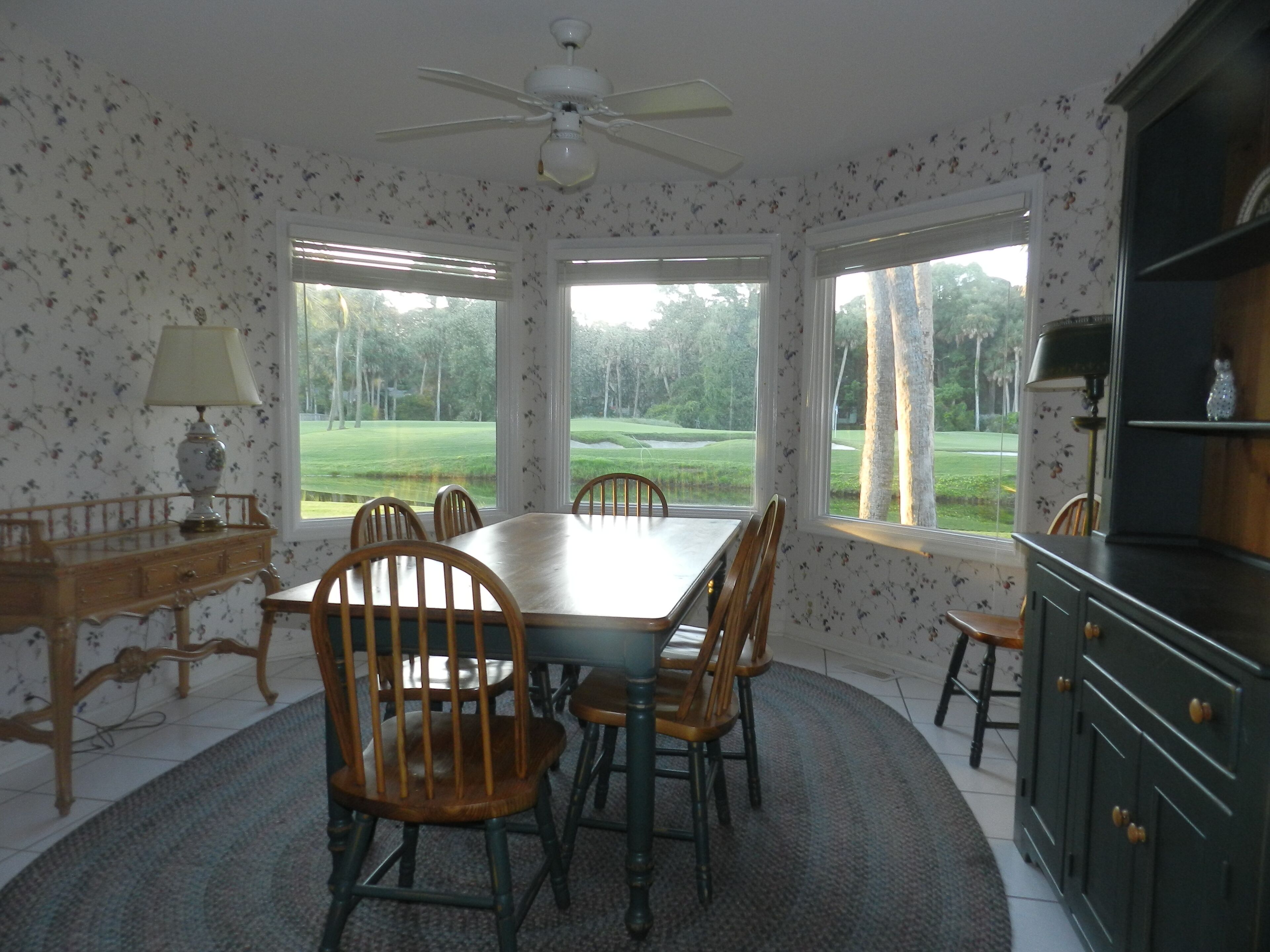 Comedor con una mesa grande, sillas, ventilador de techo y ventanas con vista a un campo de golf.