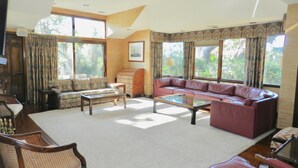 A spacious living room with a large sofa, a coffee table, and a patterned armchair. There are large windows with curtains, a wooden cabinet, and a framed picture on the wall. - Rates Jan through mid March 2027 are reduced for longer stays. (Hilton Head Island)